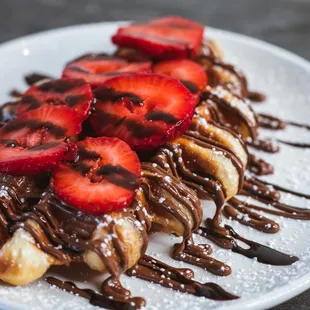 a plate of crepes with chocolate sauce and strawberries