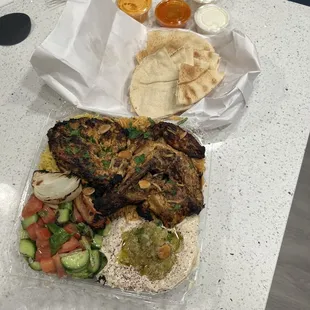 Half chicken with salad, rice, hummus, and sauces.