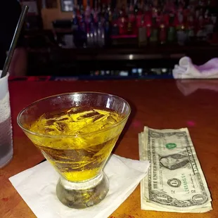 a glass of liquid and a dollar bill on a bar counter