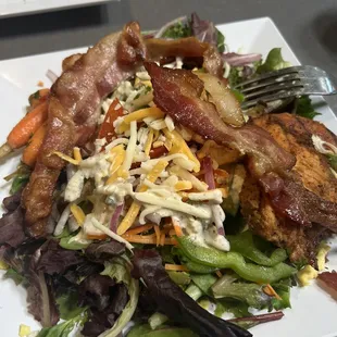 a plate of salad with bacon, lettuce, carrots, and other vegetables