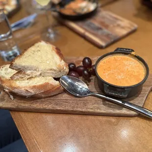 a wooden board with bread, grapes, and a bowl of soup