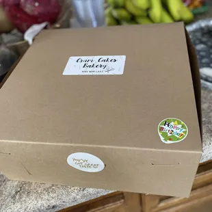 Cardboard cake delivery box with &quot;Crum Cakes Bakery, made with care,&quot; &quot;Happy Birthday!&quot;, and &quot;You&apos;ve got great taste&quot; stickers.