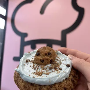 a hand holding a chocolate chip cookie with cream frosting