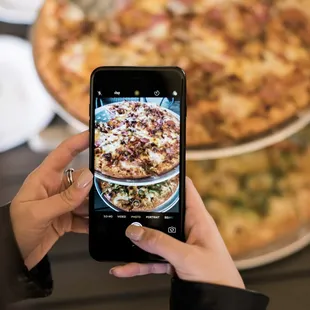 a woman taking a picture of a pizza