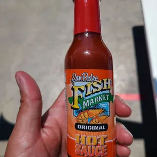 a hand holding a bottle of hot sauce