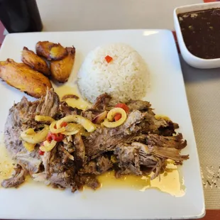 Roasted pork with Mojo on top and included sides of rice, sweet plantains, and black beans