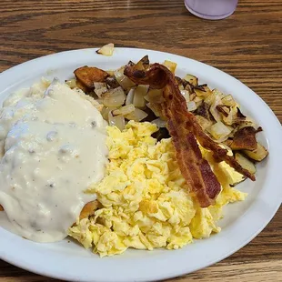 Biscuits and gravy breakfast, with bacon, potatoes, and scrambled eggs.