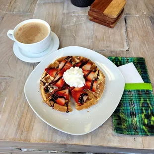 Yummy waffle with strawberries, whipped cream, and chocolate syrup. and a chai tea latte with oat milk