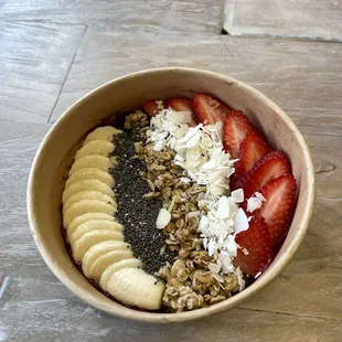 Acai bowl topped with fresh banana, strawberries, chia seeds, granola, coconut flakes, and honey. Also available vegan and gluten free.