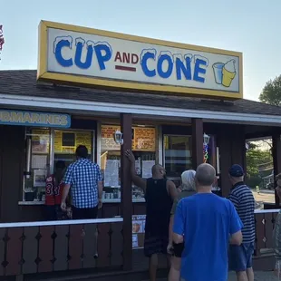 a group of people standing outside of a cup and cone