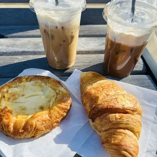 a croissant, coffee, and pastry on a picnic table