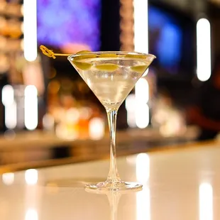 a martini with olive garnish sitting on a bar