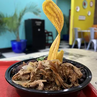 Lechon asado bowl with plantain chip on top.