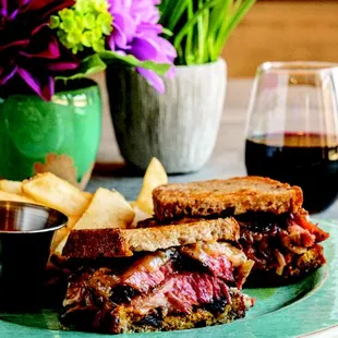 a grilled beef sandwich with chips and a glass of wine