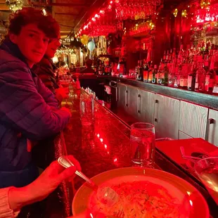 a woman sitting at a bar with a bowl of soup in front of her