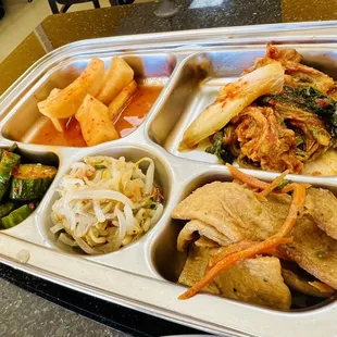 Side dishes of three different kinds of kimchis, bean sprouts and fish cakes
