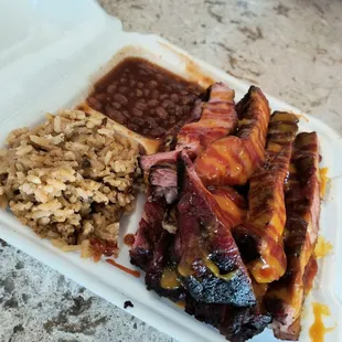 a white styrofoam container with ribs, beans, rice, and beans