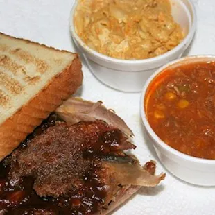 a grilled beef sandwich with a side of beans and coleslaw