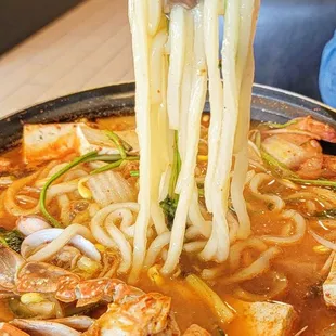 a person lifting noodles from a skillet