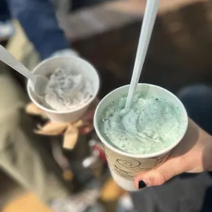 a person holding two cups of ice cream