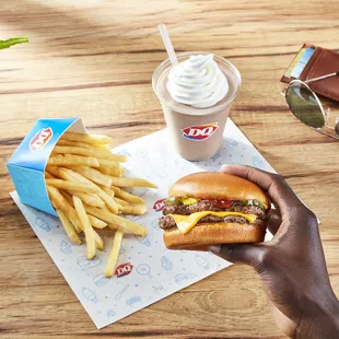 a hand holding a cheeseburger and fries