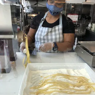 a woman in a mask and apron making pasta