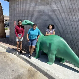 three people standing next to a fake dinosaur