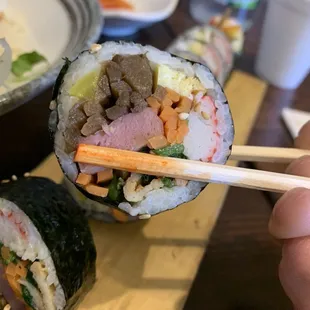 a person holding chopsticks over a sushi