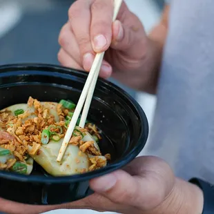 a person holding a bowl of food with chopsticks