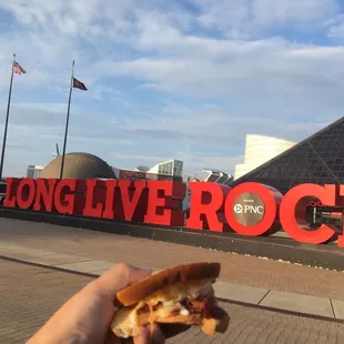 a hand holding a sandwich in front of the long live rock sign