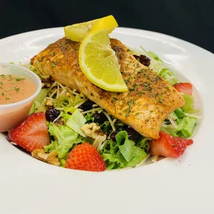 a plate of salad with chicken, strawberries, and a lemon wedge