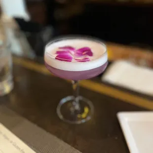 a purple cocktail sitting on a bar