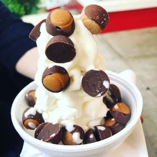 a person holding a bowl of ice cream and chocolate covered nuts