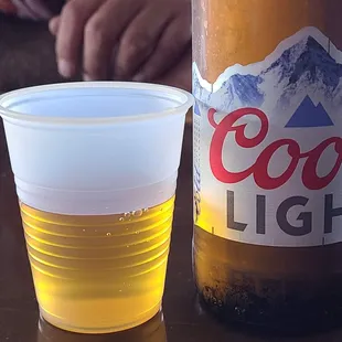 a bottle of coors light next to a plastic cup