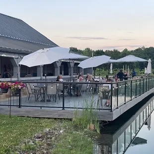 a group of people sitting at tables on a deck overlooking a lake