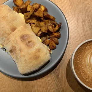 Egg, bacon, and cheese sandwich with cappuccino and side of potatoes