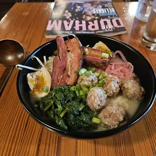 a bowl of ramen with meatballs, broccoli, and eggs