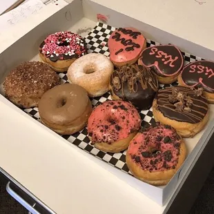 A dozen donuts with a few of their special Valentine's Day theme decorated ones.