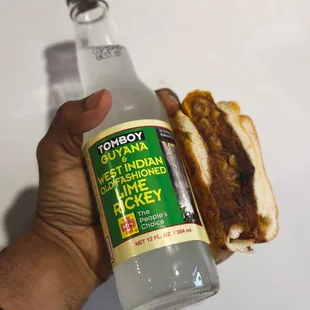 a hand holding a bottle of soda and a hot dog