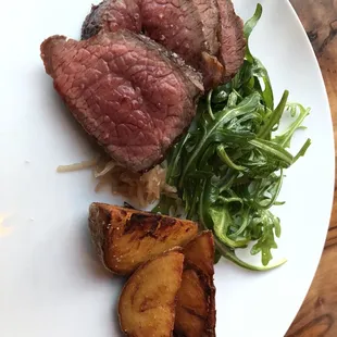 Steak with potato wedges and arugula salad