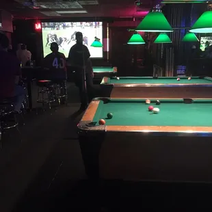 One side of the fairly large dive bar with several billiards tables and screens to watch the game