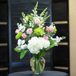 Elegant white hydrangeas, pink roses, white snap dragons and green spider mums are arranged in a ginger vase...