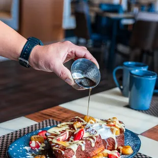 a person pouring syrup over a plate of french toast