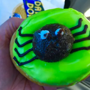 a hand holding a green frosted spider donut