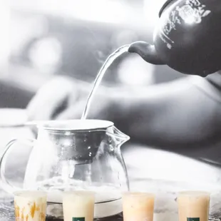 three cups of bubble tea being poured into a teapot