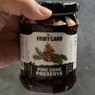 a hand holding a jar of fruitland pine cone preserve