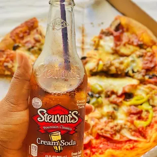 a hand holding a bottle of ice cream soda with a slice of pizza in the background