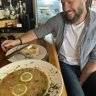 a man sitting at a bar with a plate of soup and a sandwich