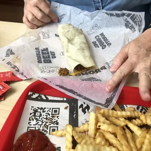 a person sitting at a table with a sandwich and french fries