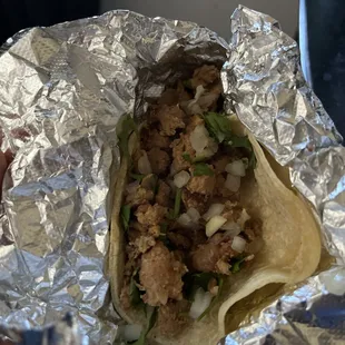 a hand holding a taco wrapped in foil
